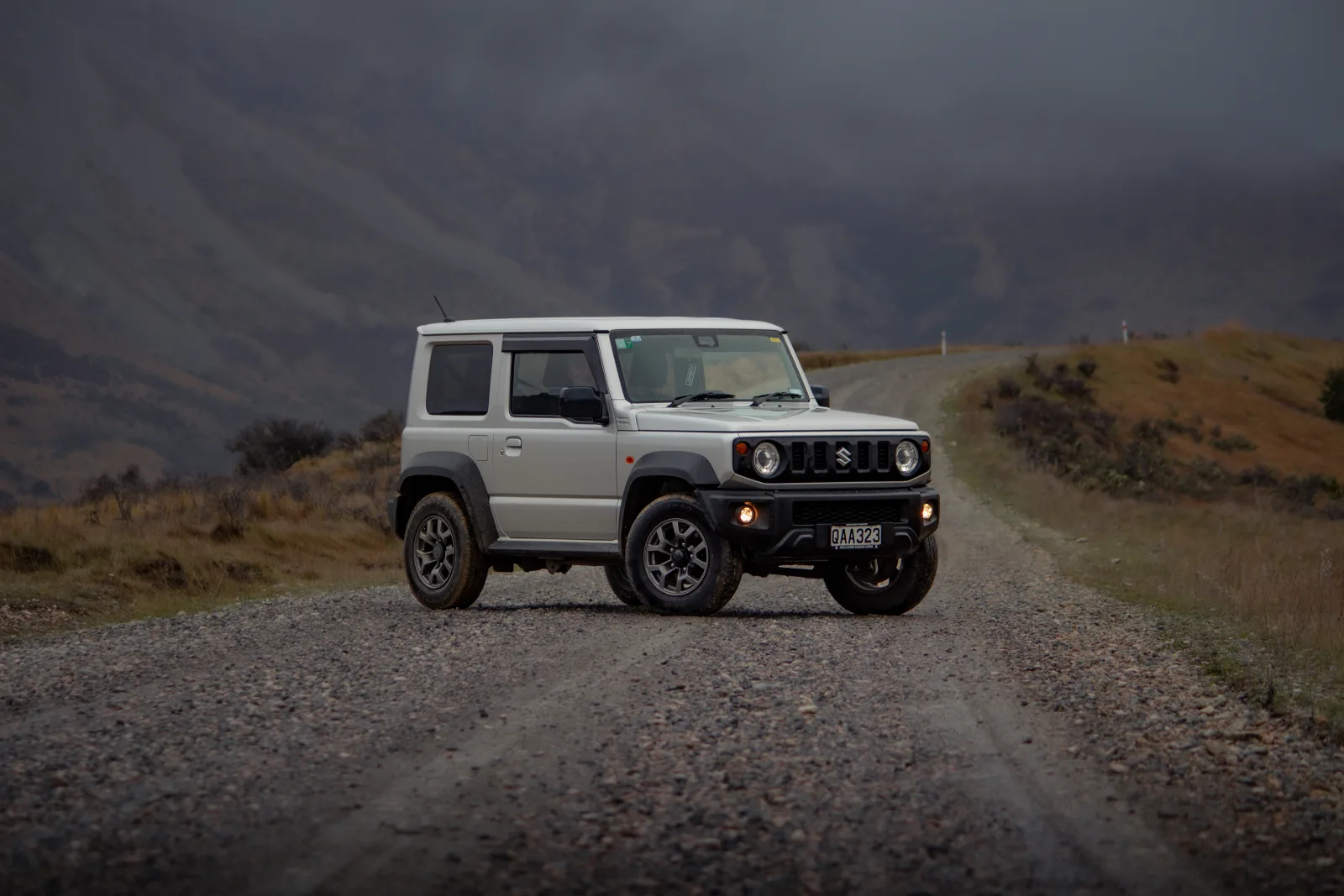 White Suzuki Jimny with rooftop tent and ladder by water at golden hour. – Jimny Rentals.