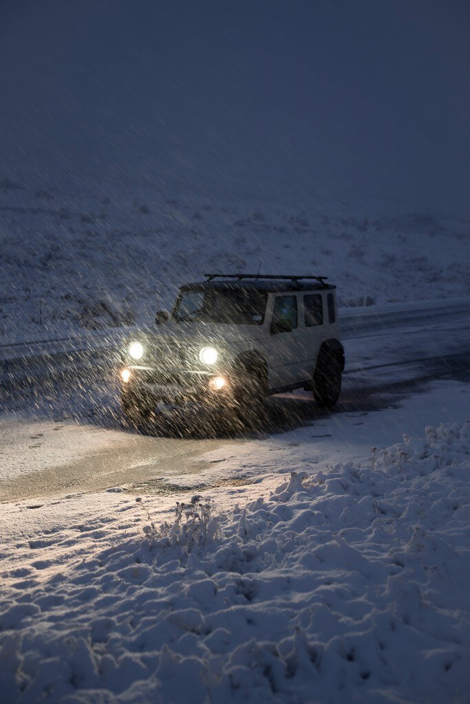 Jimny driving through blizzard at night, headlights cutting through falling snow
