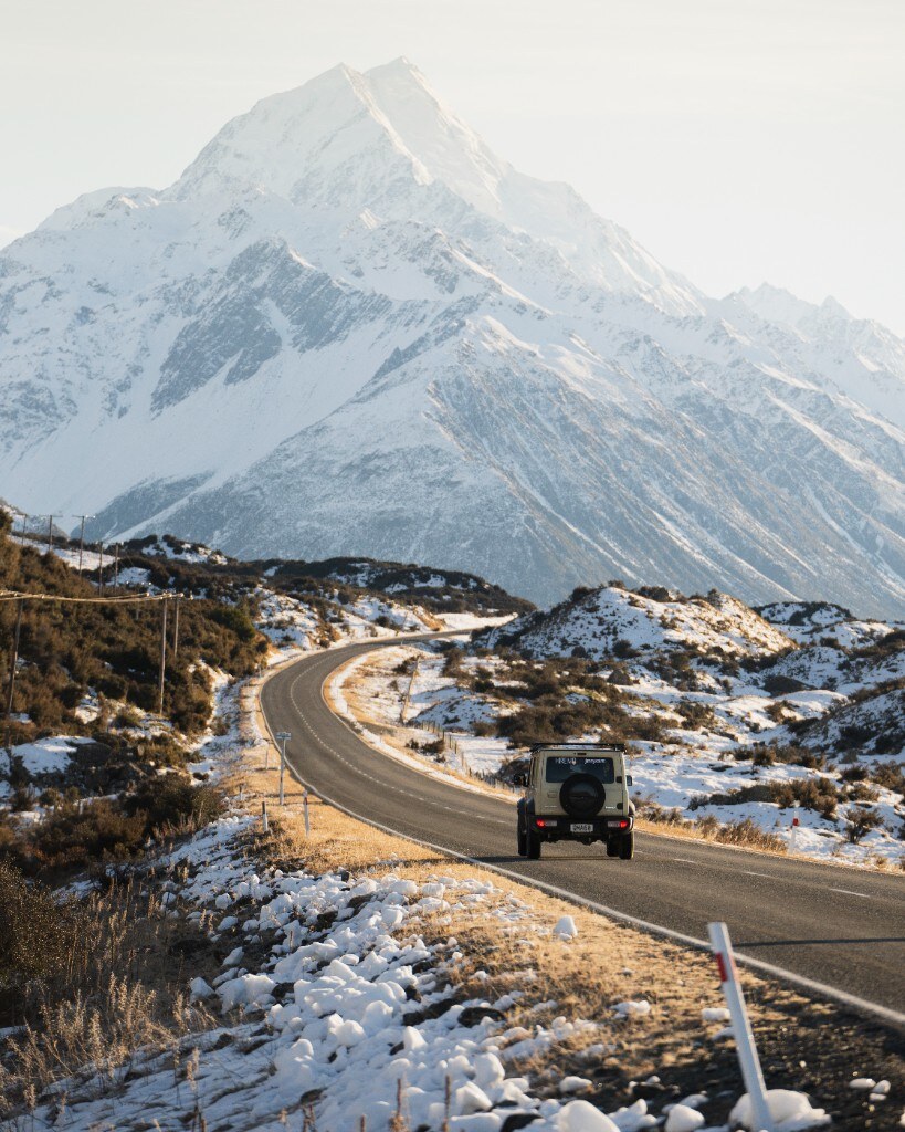 Jimny driving toward Aoraki/Mt Cook along golden Lake Pukaki road at winter sunrise