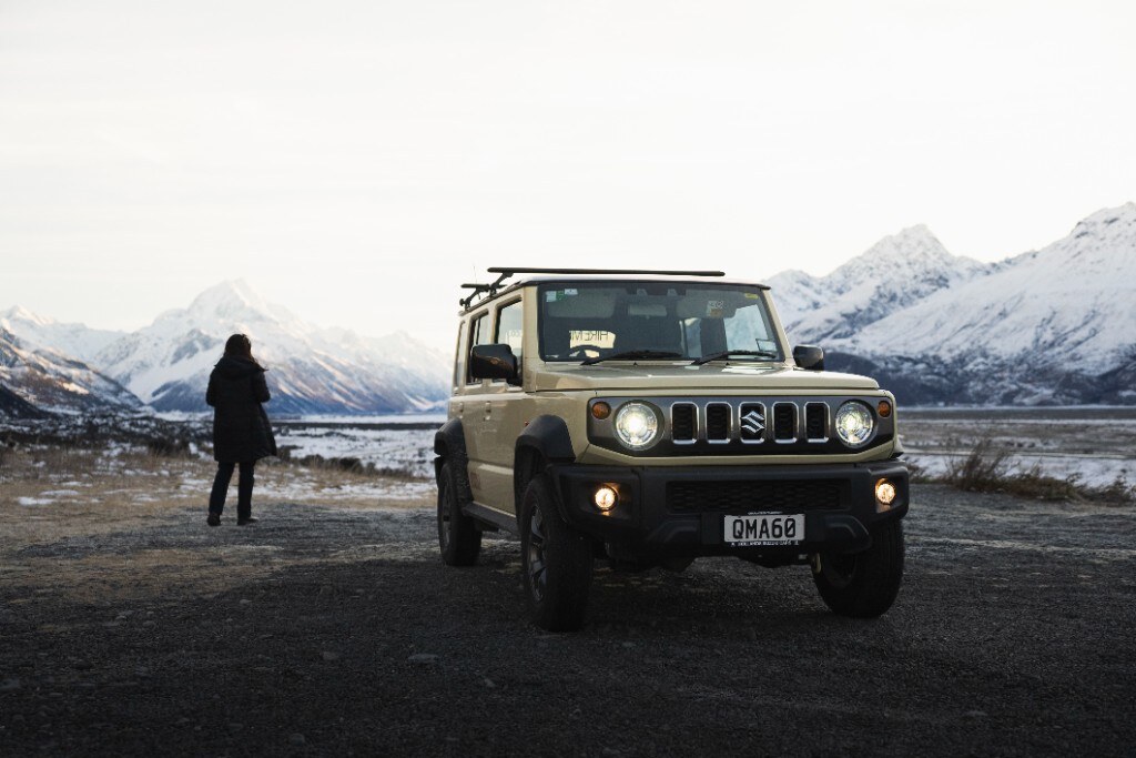 Person standing outside Jimny at frozen lake with Mt Cook behind