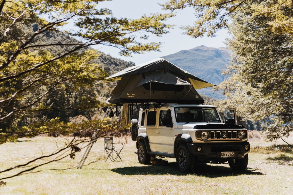 Jimny with rooftop tent in scenic landscape.