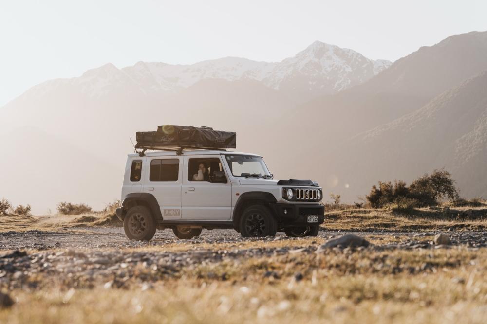 A Jimny at golden hour on a gravel pull off with snow capped ranges beyond