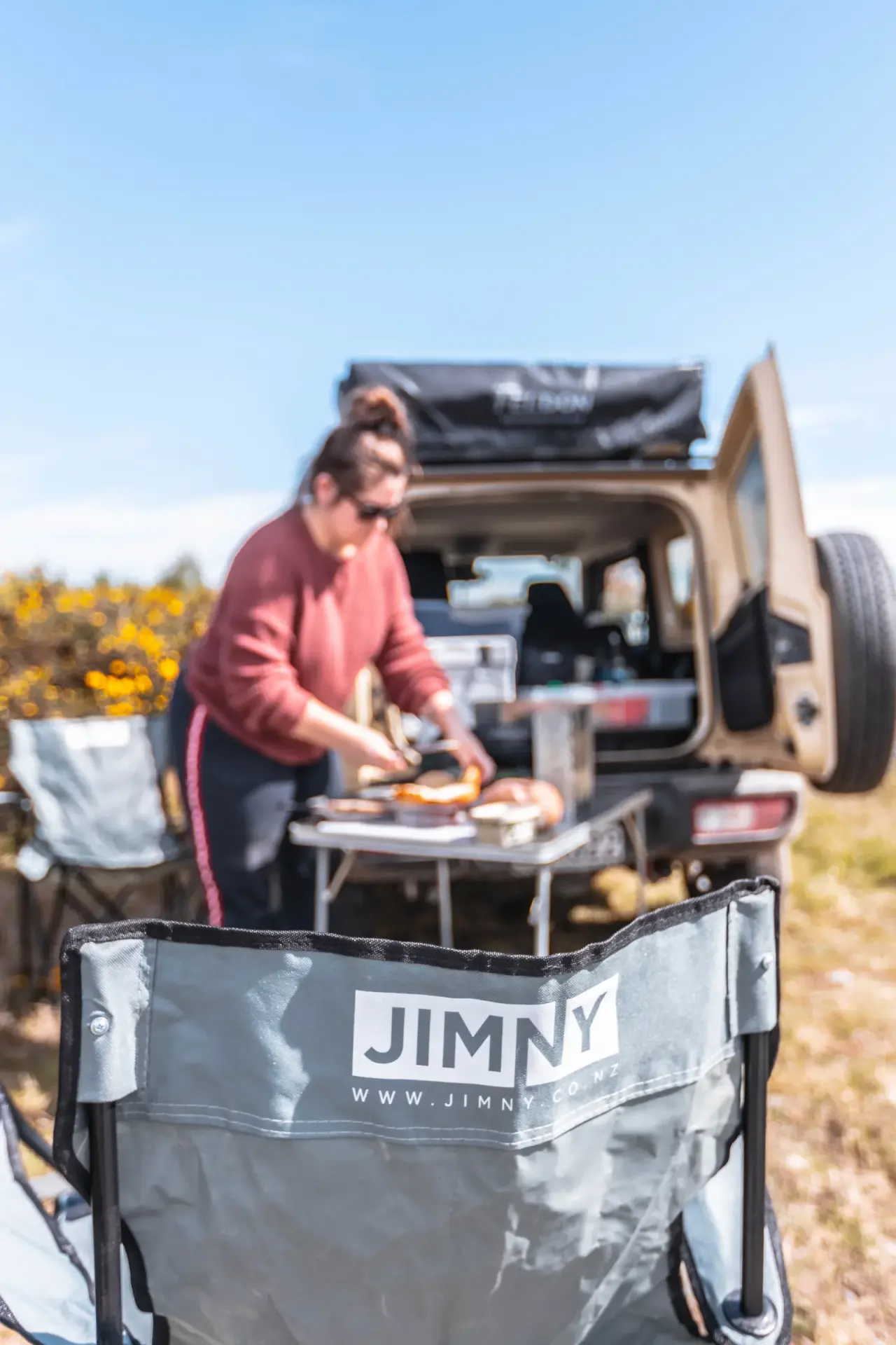 Woman photographing mountains with white Jimny and rooftop tent, scenic road. – Jimny Rentals.