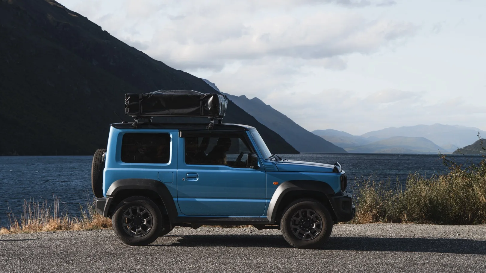 Suzuki Jimny on a snowy gravel track with snow-capped mountains