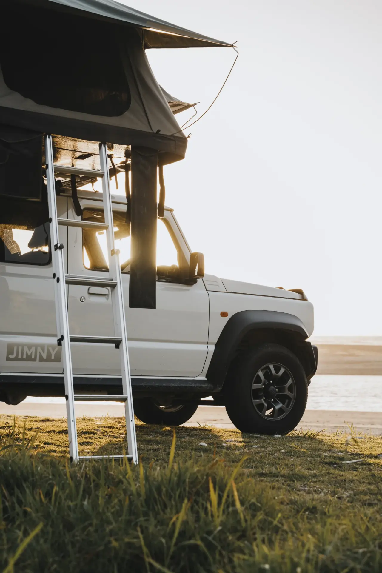 Suzuki Jimny with rooftop tent and ladder, camping setup. – Jimny Rentals.